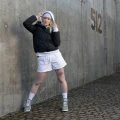 Osoba w sportowej stylizacji – biała bluza z kapturem, czarna pikowana kurtka, białe szorty, długie białe skarpetki Basic Arctic Snow i szare sneakersy.