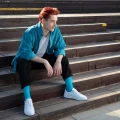 Młody mężczyzna w morskich skarpetkach i białych sneakersach siedzi na drewnianych schodach w stylizacji streetwear.