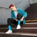 Mężczyzna siedzący na schodach, w morskich skarpetkach, poprawiający nogawkę koszuli.