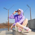 Kobieta w liliowych skarpetkach Basic - French Lavender, różowo-białych sneakersach i fioletowej bluzie z kapturem siedzi na betonowym murku w słoneczny dzień.
