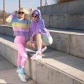Dwie kobiety w pastelowych stylizacjach stoją na betonowych schodach. Jedna w liliowych skarpetkach i różowych sneakersach, druga w błękitnych skarpetkach i białych butach sportowych.