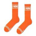 Pomarańczowe skarpetki sportowe z białymi detalami i napisem „NINETIES” na ściągaczu. Utrzymane w minimalistycznym, energetycznym stylu.