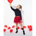 Dziewczynka w czerwonej spódniczce trzymająca czerwony balon, ubrana w czarne skarpetki dziecięce mixTURY Miłosne z motywem ust i serc, na tle rozsypanych czerwonych balonów.