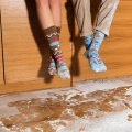 Dwie osoby siedzące na blacie kuchennym, w świątecznych skarpetkach. Jedna w brązowych przypominających piernik, druga w niebieskich z motywem świątecznych ciastek i kubków. Na podłodze rozsypana mąka.