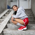Kobieta pozuje na schodach w melanżowych, długich skarpetkach "NINETIES” z białym logo i uśmiechem. Skarpetki są grubsze, sięgają do połowy łydki i świetnie komponują się z czerwonymi butami.