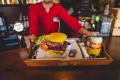 Podany na tacy kolorowy zestaw skarpet ułożonych jak burger, obok warzyw i napoju.