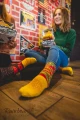 Zbliżenie na kolorowe skarpetki inspirowane burgerem, noszone przez osobę siedzącą na podłodze w stylowym, retro wnętrzu.