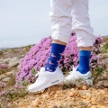 Zestaw skarpet mixTURY Pink Flamingo w różowo-niebieskiej kolorystyce, zaprezentowanych na nogach osoby w białych sneakersach, stojącego na kamienistym terenie z fioletowymi kwiatami w tle.