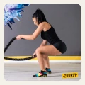 Kobieta w trakcie ćwiczeń z linami treningowymi na sali fitness, ubrana w czarny top i spodenki, na stopach kolorowe skarpetki z antypoślizgowym spodem ABS w żółtym kolorze