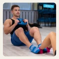 Mężczyzna w sportowych niebieskich skarpetkach z antypoślizgowym spodem ABS ćwiczy na macie w siłowni; trzyma talerz treningowy i wykonuje ćwiczenia na mięśnie brzucha.