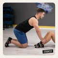 Mężczyzna w sportowym stroju klęczy na podłodze siłowni, trzymając nogi partnerki wykonującej brzuszki; oboje mają na sobie czarne skarpetki z kolorowym wzorem i antypoślizgowym spodem ABS.