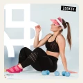 Uśmiechnięta kobieta w sportowym stroju siedzi na macie treningowej, ubrana w różowe antypoślizgowe skarpetki z ABS, obok leżą niebieskie hantle.