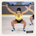 Kobieta w limonkowym topie wykonująca przysiad z gryfem, w granatowo-morskich skarpetkach antypoślizgowych z żółtym akcentem; zajęcia fitness na sali treningowej.