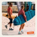 Mężczyzna z longboardem i kobieta niosąca deskę surfingową w niebieskim pokrowcu idą brzegiem plaży, oboje w kolorowych skarpetkach z letnimi motywami