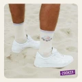 Mężczyzna w białych sneakersach i beżowych skarpetkach z napisem ‘POWER’ oraz kolorowym symbolem yin-yang, stojący na piasku