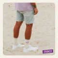 Mężczyzna stojący tyłem na plaży w białych sneakersach i kremowych skarpetkach z napisem ‘POWER’ oraz symbolem yin-yang; ubrany w dżinsowe szorty i fioletowy T-shirt.