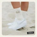 Zbliżenie na białe skarpetki  z brązowym wzorem słońca, założone do białych sneakersów, stopy stoją na jasnym piasku