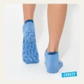 Dziecięce skarpetki stopki w kolorze jasny jeans, z antypoślizgowym spodem ABS, ujęcie od tyłu na stopach dziecka stojącego na białym tle.