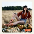 Modelka siedząca w polu wśród dyni, ubrana w pomarańczową bluzkę i jeansowe szelki, ma na sobie pomarańczowe skarpetki mixTURY Święto Dziękczynienia z jesiennym wzorem inspirowanym kapeluszami pielgrzymów i świątecznym stołem.