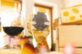 Skarpetka w serowy wzór z motywem myszy na palcach, sfotografowana w ciepłym świetle obok kieliszka czerwonego wina i dekoracji przypominających żółty ser.