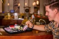 Mężczyzna trzymający pałeczkami zwiniętą skarpetkę stylizowaną na sushi nad zestawem skarpet ułożonych jak różne rodzaje sushi w restauracyjnym wnętrzu.