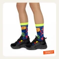 Kolorowe skarpetki w neonowo-niebiesko-czerwony pikselowy wzór i czarne sportowe buty na nogach modelki stojącej bokiem.