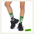 Dziecięce nogi w czarnych sneakersach i neonowo-zielonych skarpetkach z geometrycznym, pikselowym wzorem.