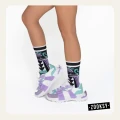 Nogi osoby w pastelowych sneakersach w odcieniach fioletu i mięty oraz artystycznych skarpetkach z geometrycznym wzorem w czerni, fiolecie i turkusie.