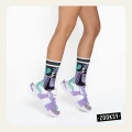 Nogi osoby w pastelowych sneakersach w odcieniach mięty, fioletu i bieli oraz artystycznych skarpetkach z geometrycznym wzorem, uchwycone w dynamicznej pozie.