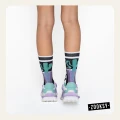 Nogi osoby widziane od tyłu w pastelowych sneakersach w odcieniach mięty i fioletu oraz artystycznych skarpetkach z geometrycznym wzorem.