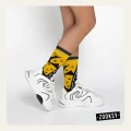 Nogi osoby w białych sneakersach i żółto-czarno-białych skarpetkach z graficznym wzorem.